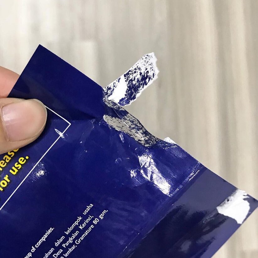 Close-up of laminated paper showing a plastic film layer being peeled off, making it unsuitable for paper recycling in Singapore.